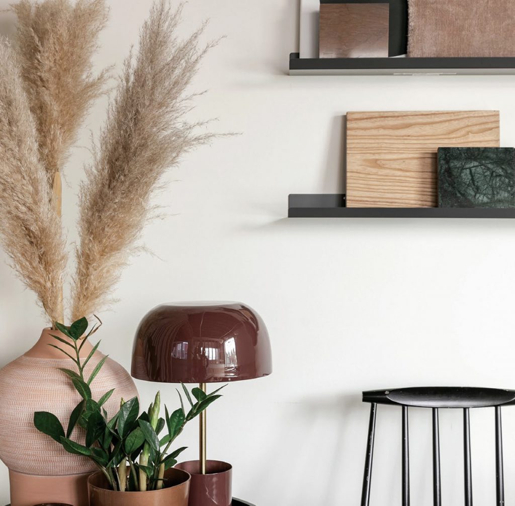 Decorative plants and lamp sit beside a stool and wall shelves. 