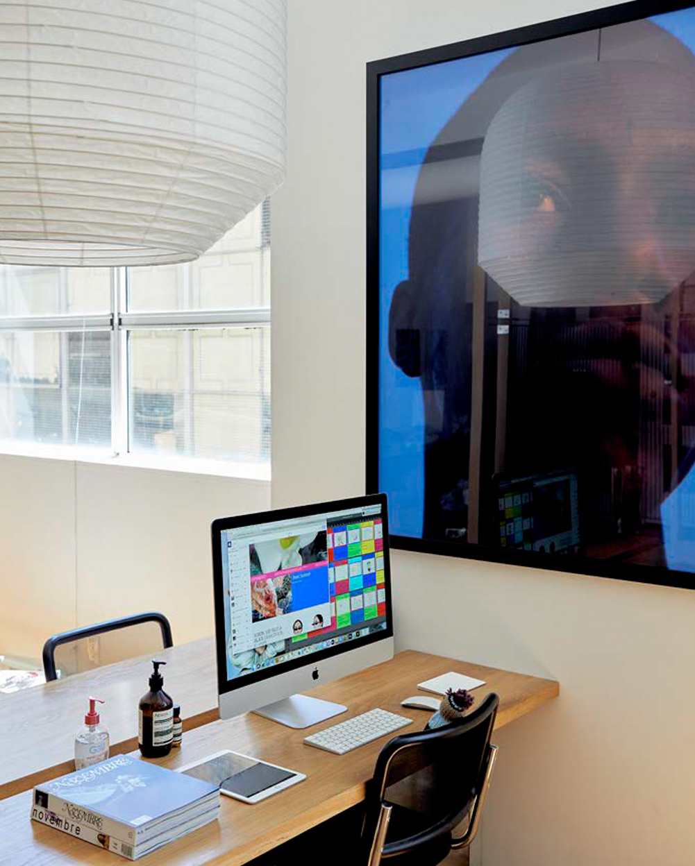 Office space with desk, mac computer, chairs and large portrait photo on wall.