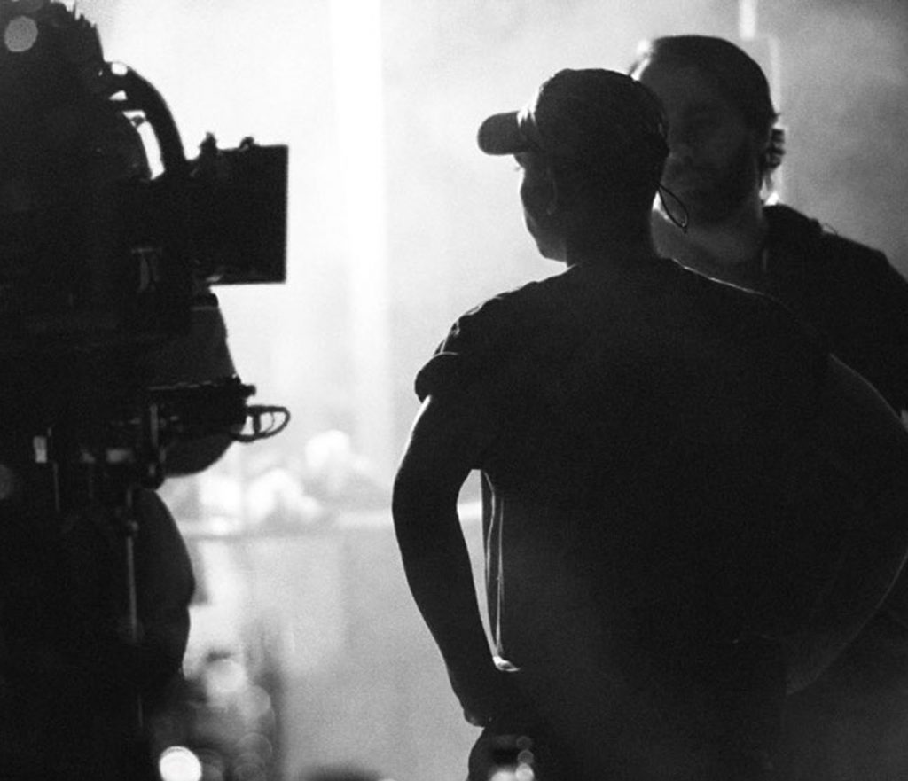 Black and white photo of filming camera and shoot directors discussing. 