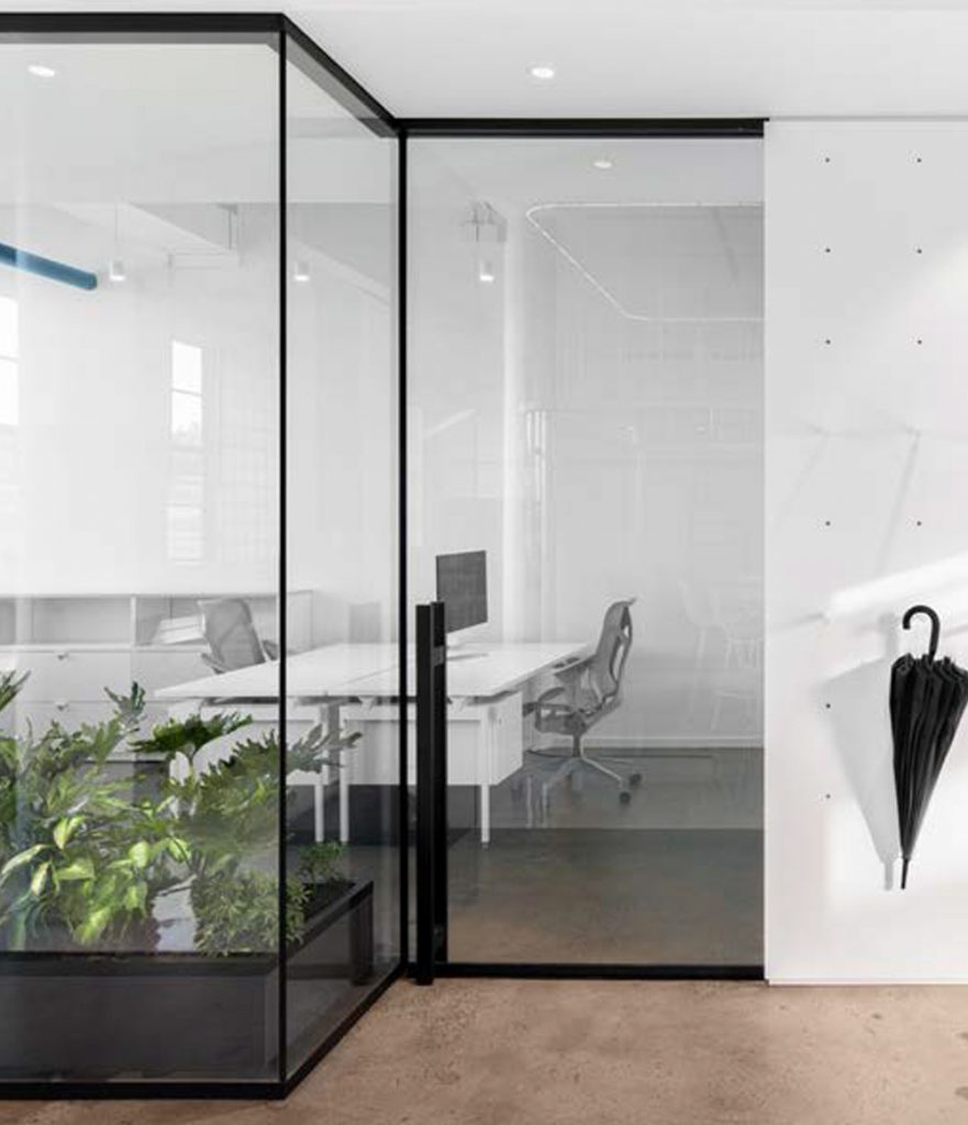 Glass meeting room with plants and white desk/chairs.