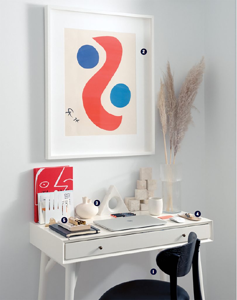 Desk set up with wall art, decorative pieces and chair in white office space. 