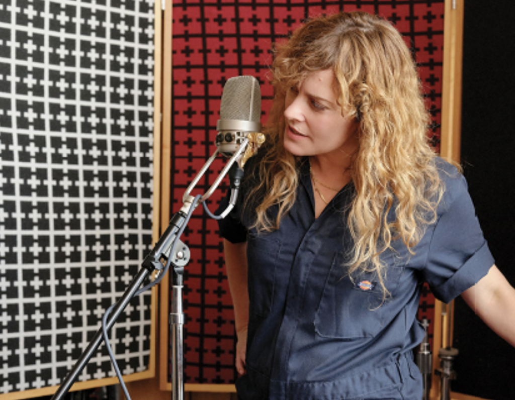 Laurel Sprengelmeyer stands by mic recording song in studio.